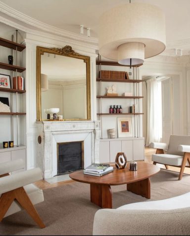 SALÓN CIRCULAR en París con una chimenea de mármol de estilo clásico, mobiliario moderno en tonos neutros y estantes de madera.